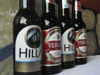 Four bottles of Greek Beer, Hillas Lager and Vergina Red Ale, on e teble with a white table cloth and with frescoed rocks as a background