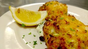 Jake and Telly's Specials - Crab Cakes. A Close up image of crab cakes on a white plate with a lemon wedge