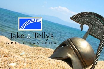 Jake & Telly's Greek Taverna: A photo of a homeric helmet in the sand on a beach with the blue ocean and blue sky visible in the background. The helmet is on teh right side of the photo and photo's horizon is at approximately a 25 degree angle and a Blue Jake and Telly's logo is present to the left of the helmet.