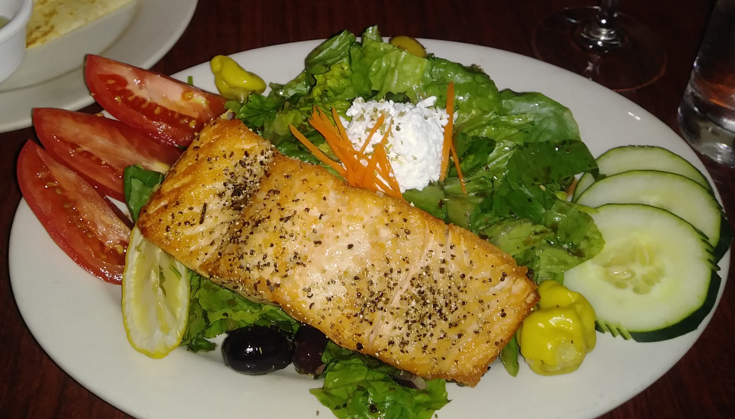 Photo of a Greek Salad with grilled Scottish Salmon on a white plate.